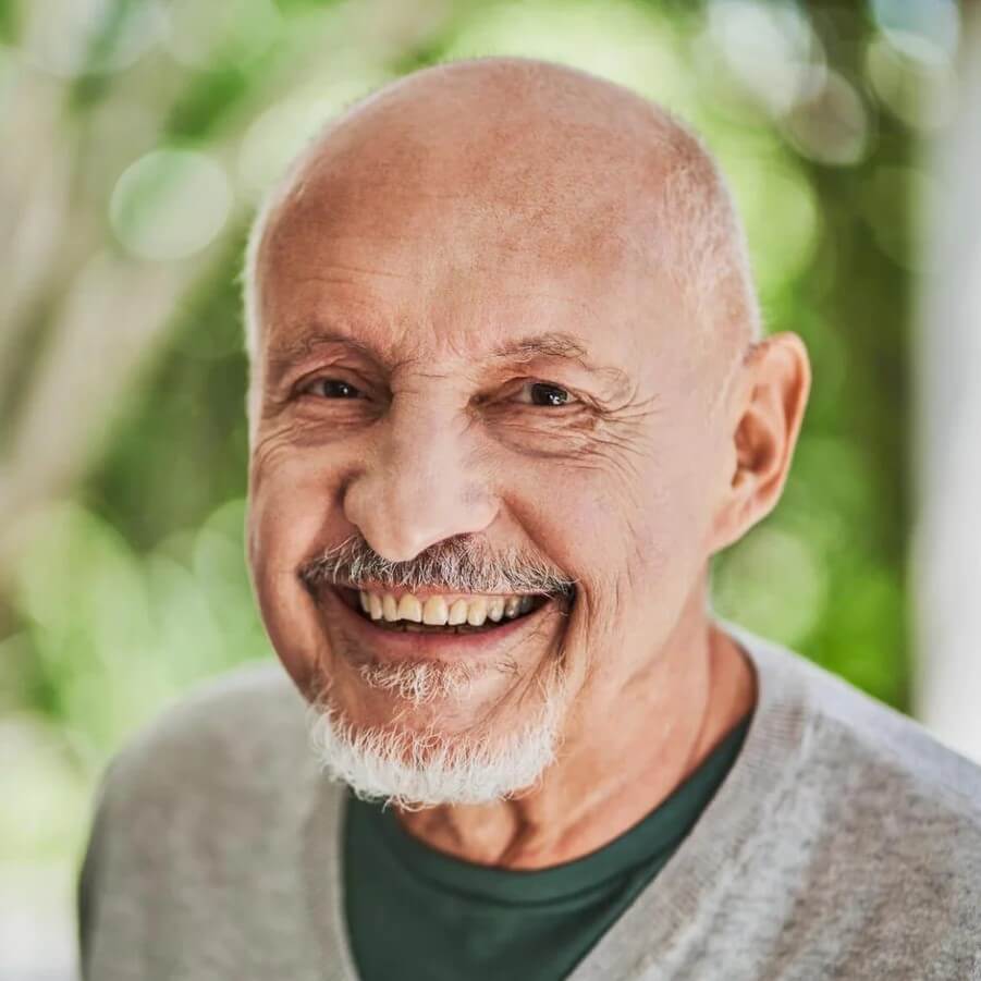 A happy middle-age man smiles for the camera in front of a natural green background.