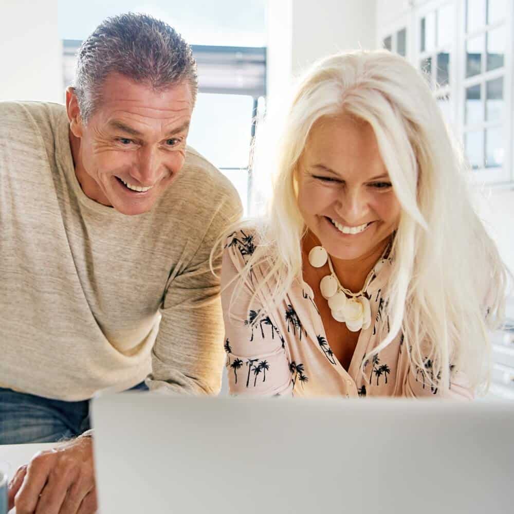 A middle-age couple look at their laptop and smile.