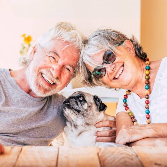 A happy older couple smile for a photo with their pug dog.
