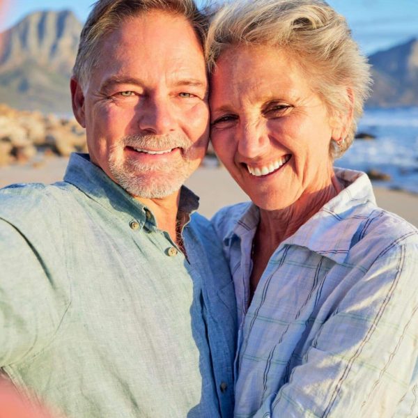 A happy couple takes a selfie on the beach as they smile in the morning sun.