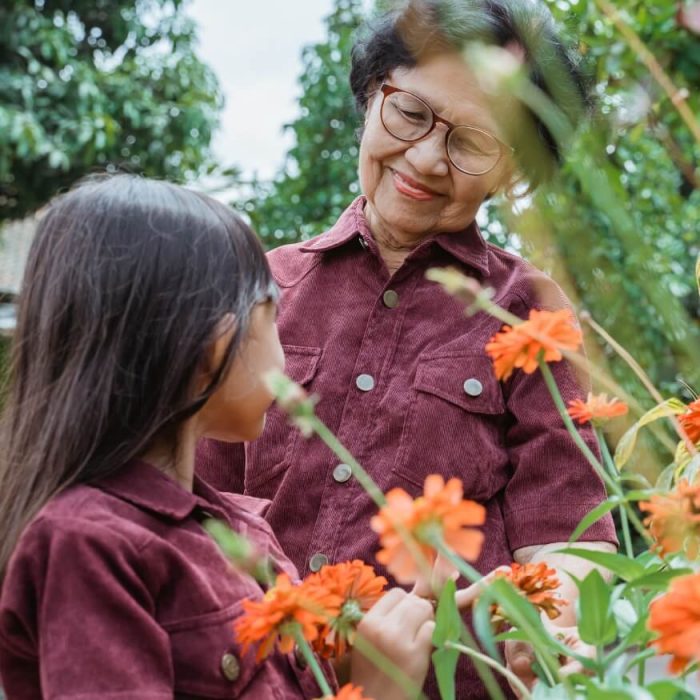 A grandmother and granddaughter look at some pretty orange flowers in the garden.